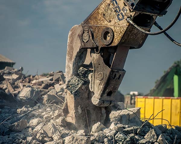 Hydraulische betonschaar aan een kraanarm knijpt een betonblok stuk